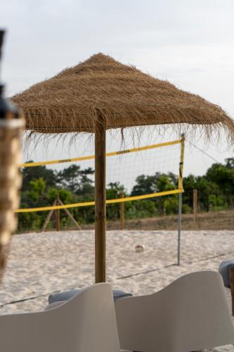 a straw umbrella on the beach with two chairs at Casa Fonte da Telha in Santiago do Cacém
