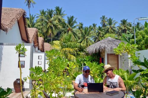 two men sitting at a table with a laptop at Nolhi Escape in Nolhivaranfaru