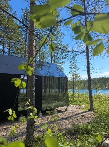 a black tent in the woods next to a lake at Sāmeland Retreat, Mirrored Glass Cabins, Swedish Lapland in Arvidsjaur