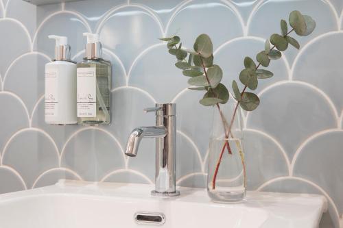 a bathroom sink with two bottles and a vase with a plant at Sigma Plus Regency Square Suites near Brighton Beach in Brighton & Hove