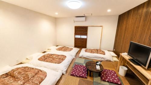 three beds in a room with a tv and a table at Takamori Guest House in Takamori