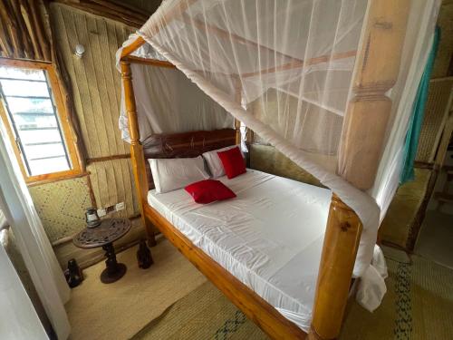 a bedroom with a canopy bed with white sheets and red pillows at Ocean view in Watamu