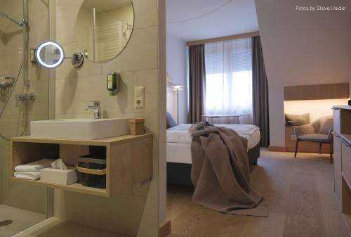 a bathroom with a sink and a shower and a bedroom at Hotel Nationalpark in Illmitz