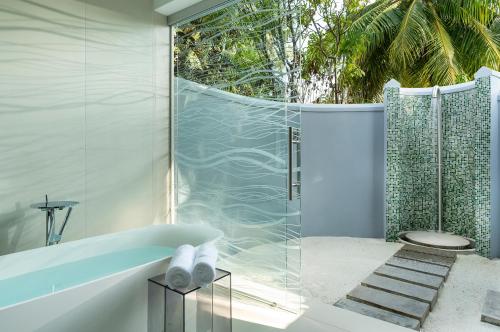 a bathroom with a tub and a glass shower at Niva Kuramathi Maldives in Rasdhoo
