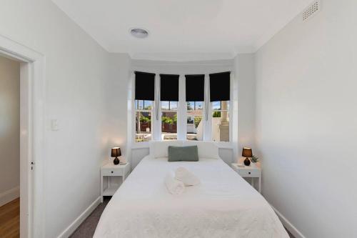 a white bedroom with a large bed and two windows at Lava House WIFI central heating cooling CBD in Warrnambool