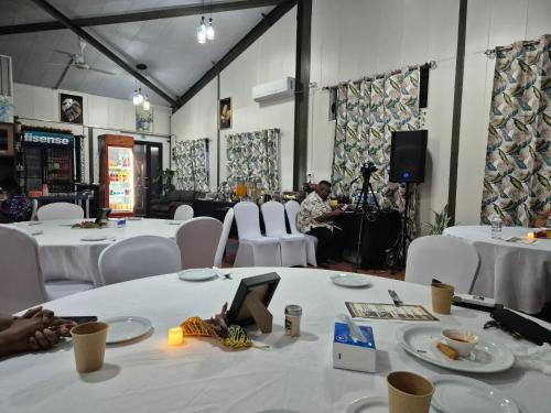 a room with white tables and white chairs and a stage at Standard - Bluelight Village Hotel in Nadi
