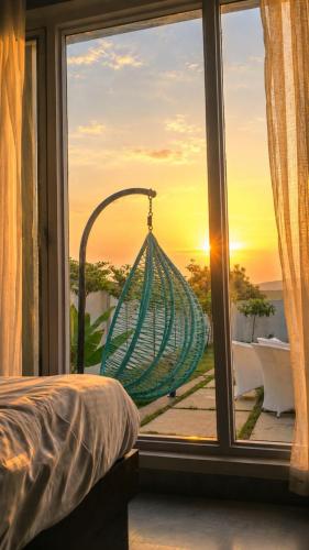 a window with a hammock looking out at the sunset at 4j Aravalli Farms in Dhauj