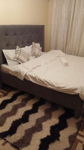 a bed with white sheets and pillows on a rug at Urban Pulse Suites in Ruiru