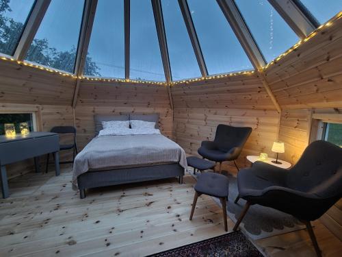 a bedroom in a wooden house with a bed and chairs at Lavvo med glasstak in Svenseid