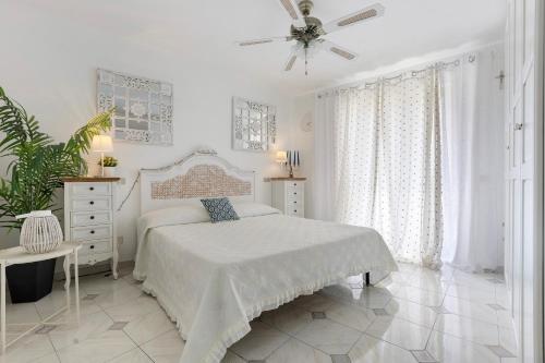 a white bedroom with a bed and a ceiling fan at A due passi dal mare in Oliveri