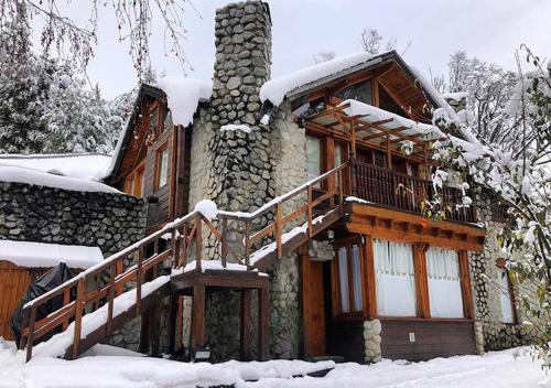 a log cabin with a snow covered porch and stairs at Ruma Andina by DOT Cabana in Villa La Angostura