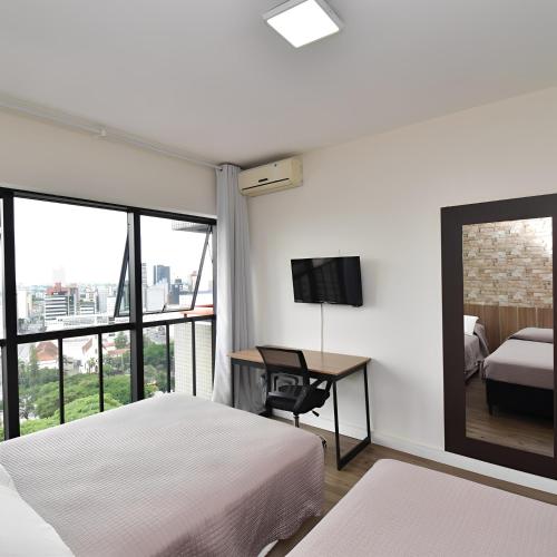a bedroom with two beds and a desk with a television at Apart 1803 - Centro Curitiba in Curitiba