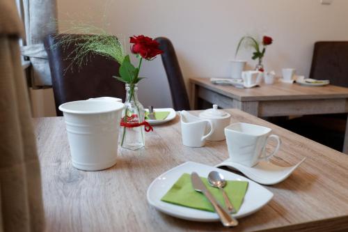 a wooden table with plates and a vase with a red rose at Pension Christina in Vaihingen an der Enz