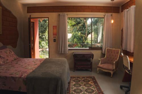 a bedroom with a bed and a window and a chair at Vila Amor - Charmosa e Central in Alto Paraíso de Goiás