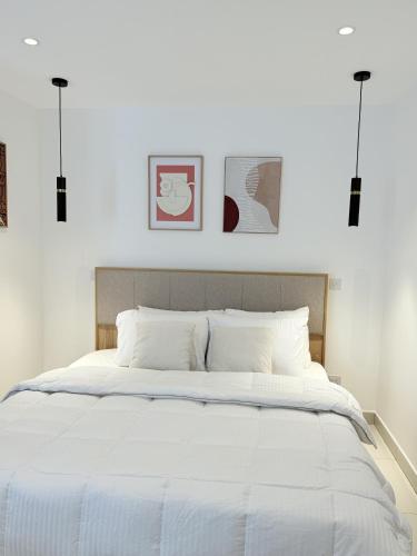 a bedroom with a large white bed with three pictures on the wall at The Lennox D-Plus Apartments in Accra