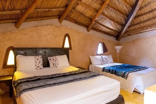 two beds in a room with wooden ceilings at Gîte Raid Oriental in Taforhalt