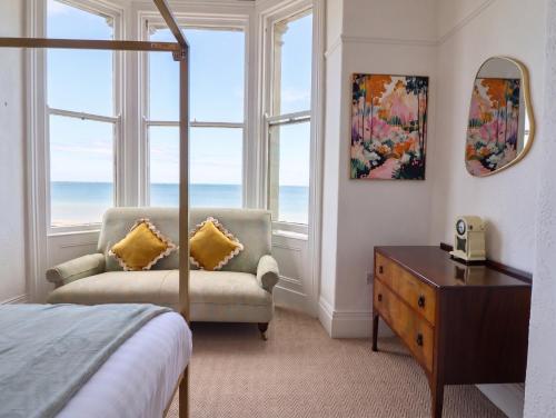 a bedroom with a bed and a chair and windows at Sea View, East Parade in Llandudno