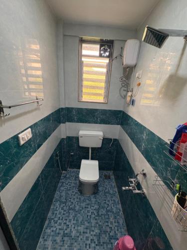 a bathroom with a toilet and green tiled walls at kailasa Villa in Karjat