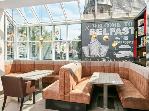 a restaurant with a couch and two tables and windows at ibis Belfast Queens Quarter in Belfast