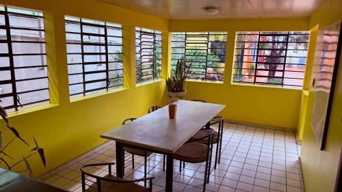 a table and chairs in a yellow room with windows at Vila Santê in Belo Horizonte