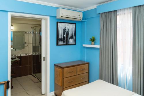 a blue bedroom with a bed and a dresser and a bathroom at Culture Crossroads Inn in Port-of-Spain