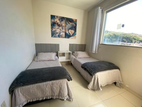 two beds in a room with a window at Apto Aconchego no Coração de Capitólio condomínio residencial in Capitólio