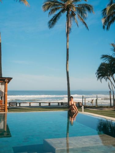 a woman sitting next to a palm tree next to a swimming pool at Olisa Al Mar in Maresias