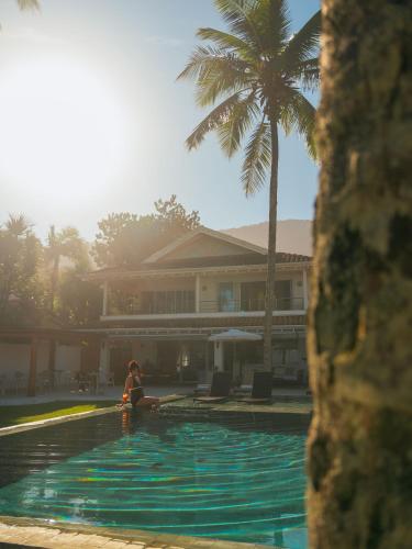 a woman sitting next to a swimming pool with a palm tree at Olisa Al Mar in Maresias