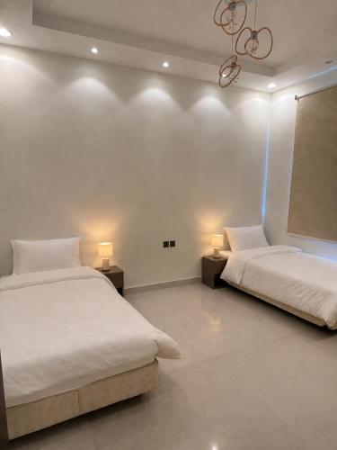 two beds in a white room with two lamps at شقه فندقه in Hail