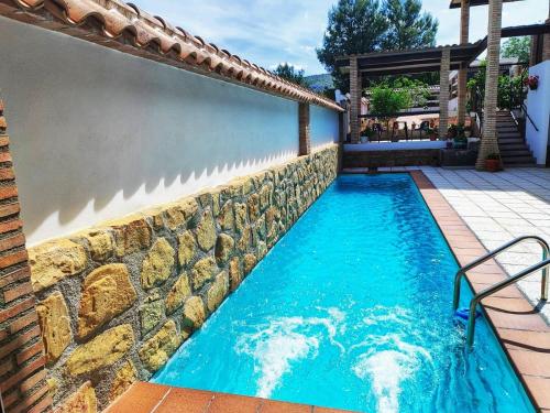 a swimming pool with a stone wall next to a house at El Pajar - Apartamento rural en la Vía Verde in Luque