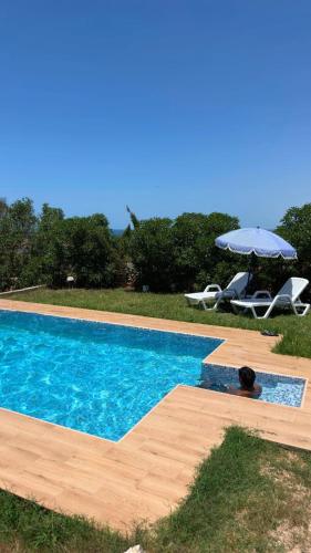 a swimming pool with an umbrella and a table and chairs at Villa Basmat in Oualidia