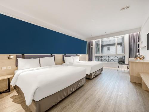 two beds in a hotel room with a blue wall at CHECK inn Select Taipei Nangang in Taipei