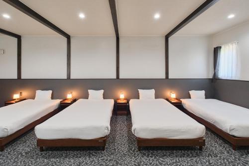 three beds in a room with lights on the wall at Aoyagi Stay in Shiomichō