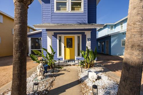 a blue house with a yellow door and palm trees at Salty Waves | Beach Cottage, Walk to Beach, Pool, Fenced Yard & Grill in Port Aransas