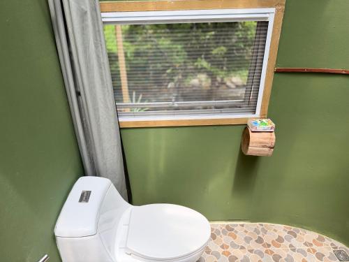 a green bathroom with a toilet and a window at The ForRest Peace Forest แม่กำปอง in Ban Huai Kaeo