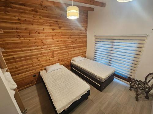 two beds in a room with a wooden wall at Cabaña Lafken in Panguipulli