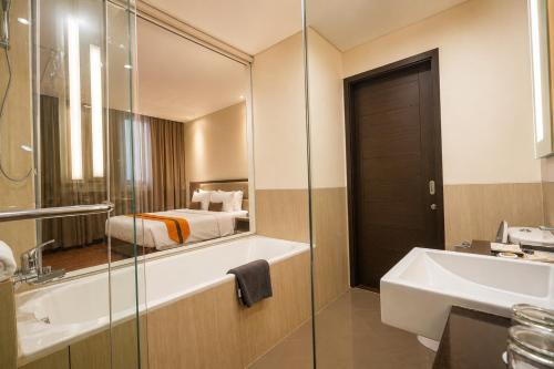 a bathroom with a tub and a sink and a bed at Oria Hotel Jakarta in Jakarta