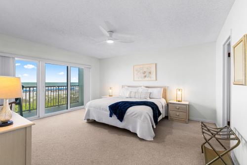 a white bedroom with a bed and a balcony at Boardwalk 201 in Cocoa Beach