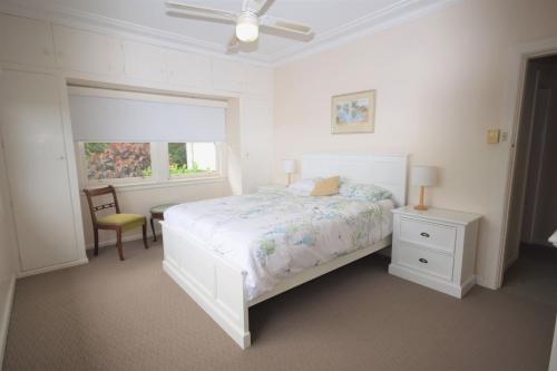a white bedroom with a bed and a chair and a window at The Outlook in Nambucca Heads