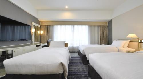 a hotel room with three beds and a flat screen tv at Hotel New Otani Makuhari in Chiba