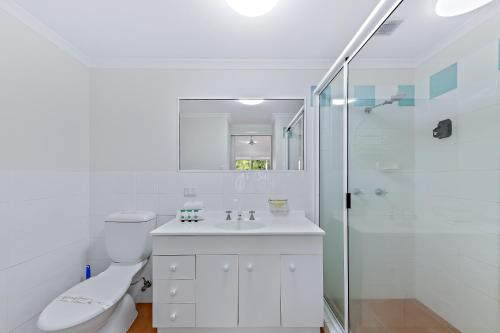 a white bathroom with a toilet and a shower at Beach Court - Airlie Beach in Airlie Beach