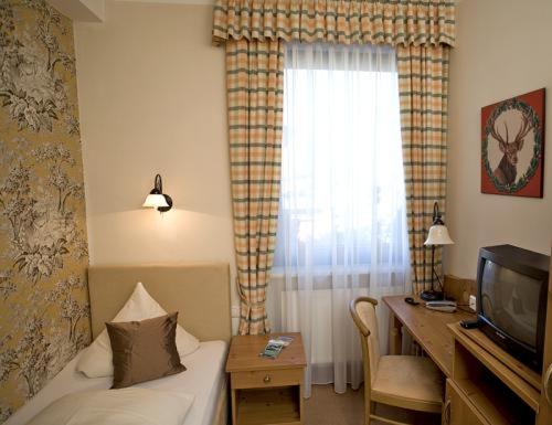 a hotel room with a bed and a desk and a television at Alpina Hotel in Rosenheim
