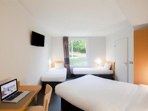 um quarto com 2 camas e um computador portátil numa secretária em B&B HOTEL Marne-La-Vallée Torcy em Torcy