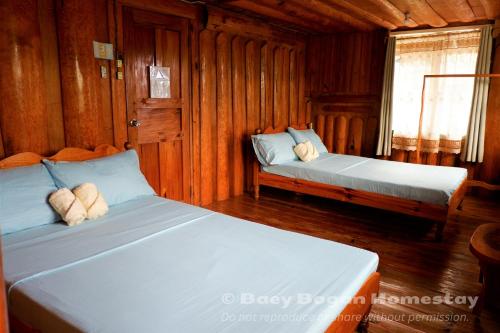 two beds in a room with wooden walls at Baey Bōgan Homestay in Sagada