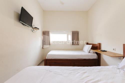 a bedroom with two beds and a tv on the wall at Nipa Guest House near Universitas Widyagama Mitra RedDoorz in Blimbing