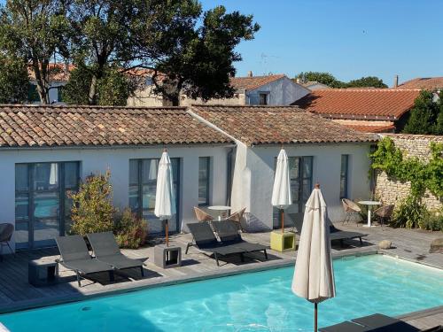 a swimming pool with two umbrellas and chairs next to a building at Hotel L'Océan in Le Bois-Plage-en-Ré
