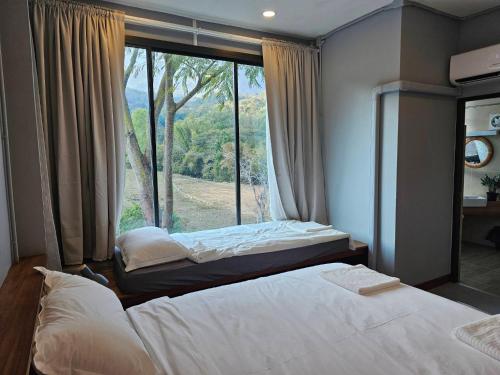 two beds in a room with a large window at Piney Stay ไพนี่สเตย์ เขาค้อ in Campson