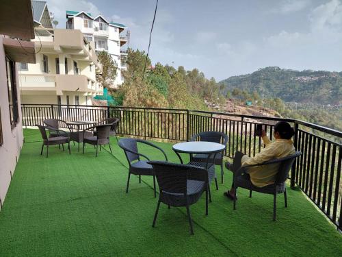 a man sitting on a balcony with a table and chairs at Villa Harrington in Barog