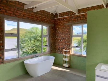 a bathroom with a large white tub and windows at The Boathouse in Harrismith