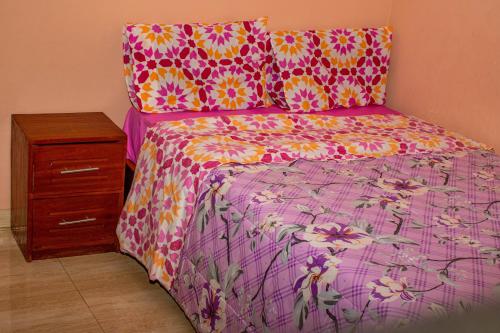 a bed with a pink and yellow bedspread and a night stand at Mailos Accommodation in Songo